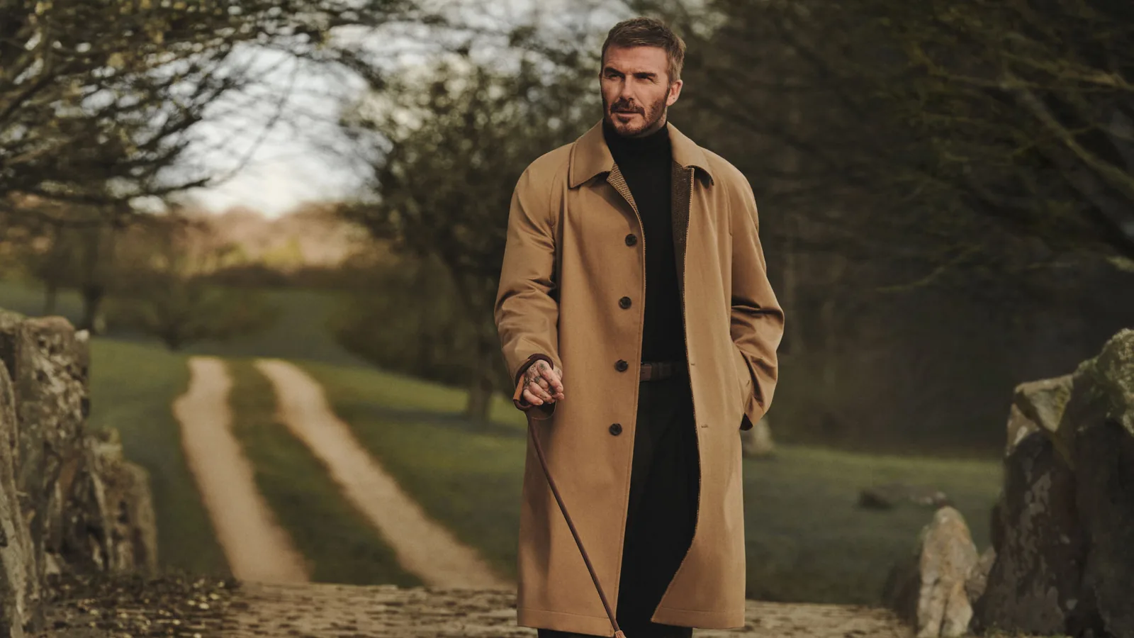 BOSS by Beckham von HUGO BOSS: David Beckham in camelfarbenem Mantel mit Hund auf einem Landweg