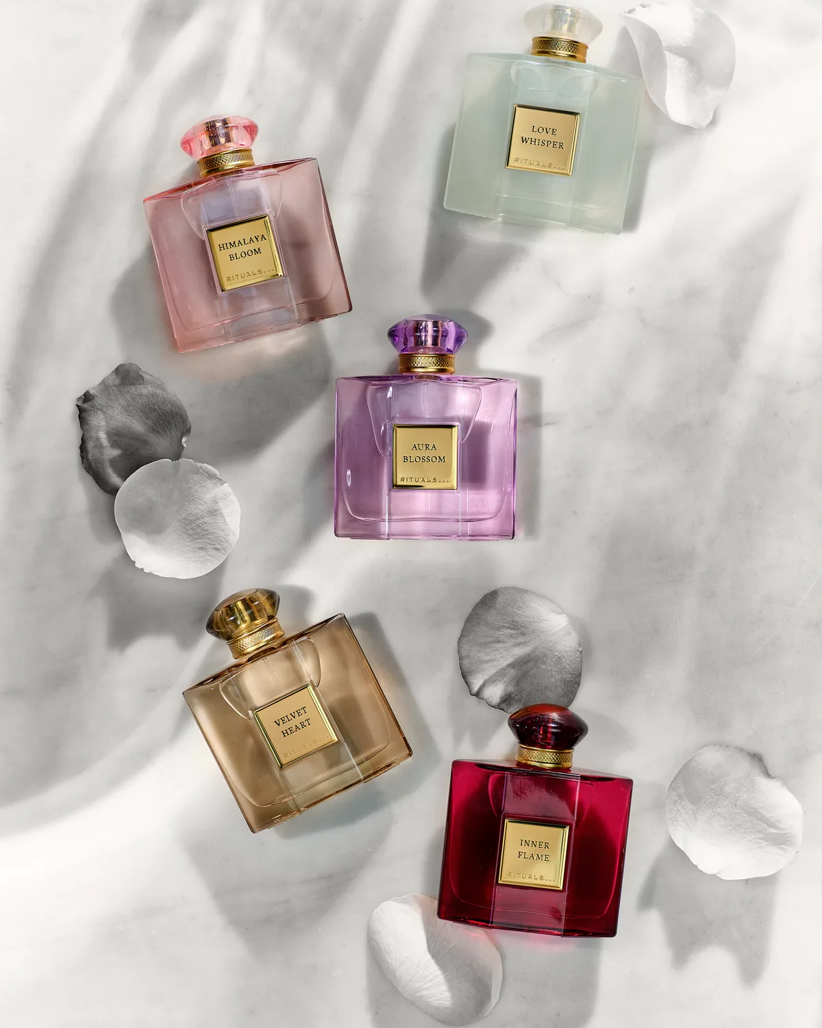 Rituals The Founder's Collection: fünf Flakons mit Blütenblättern auf hellem Stoff